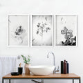 Three framed black and white botanical bathroom wall pictures above a modern wooden vanity unit