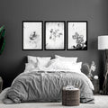 Three black and white botanical bedroom art prints hung above a grey bed