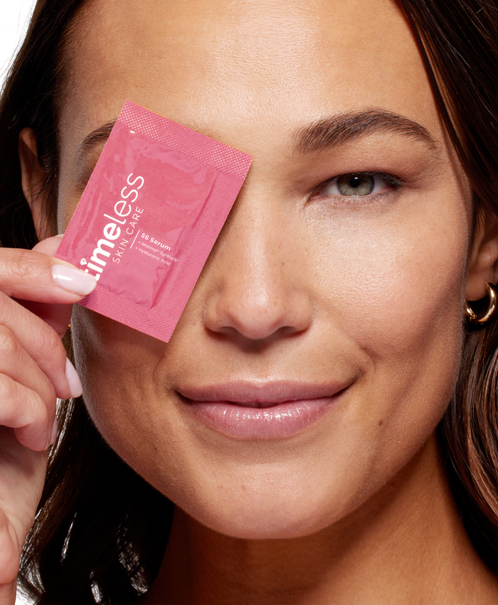 Close-up of a model holding a Timeless S6 Serum sample packet over one eye.